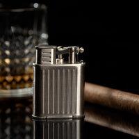 Metal lighter with a cigar and glass on a dark background